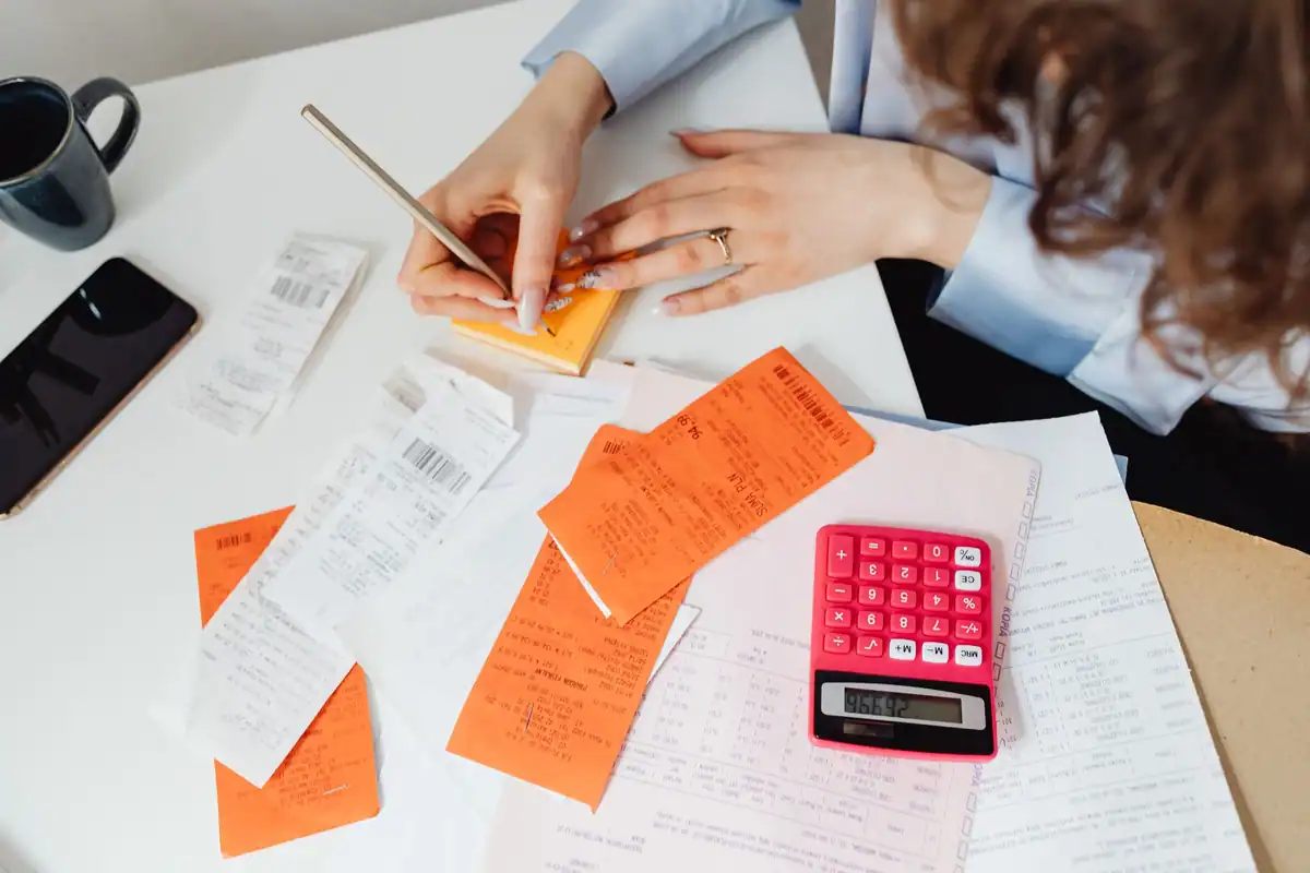 Bonuri, notițe portocalii și un calculator roz, la calculul cheltuielilor cu comisioanele