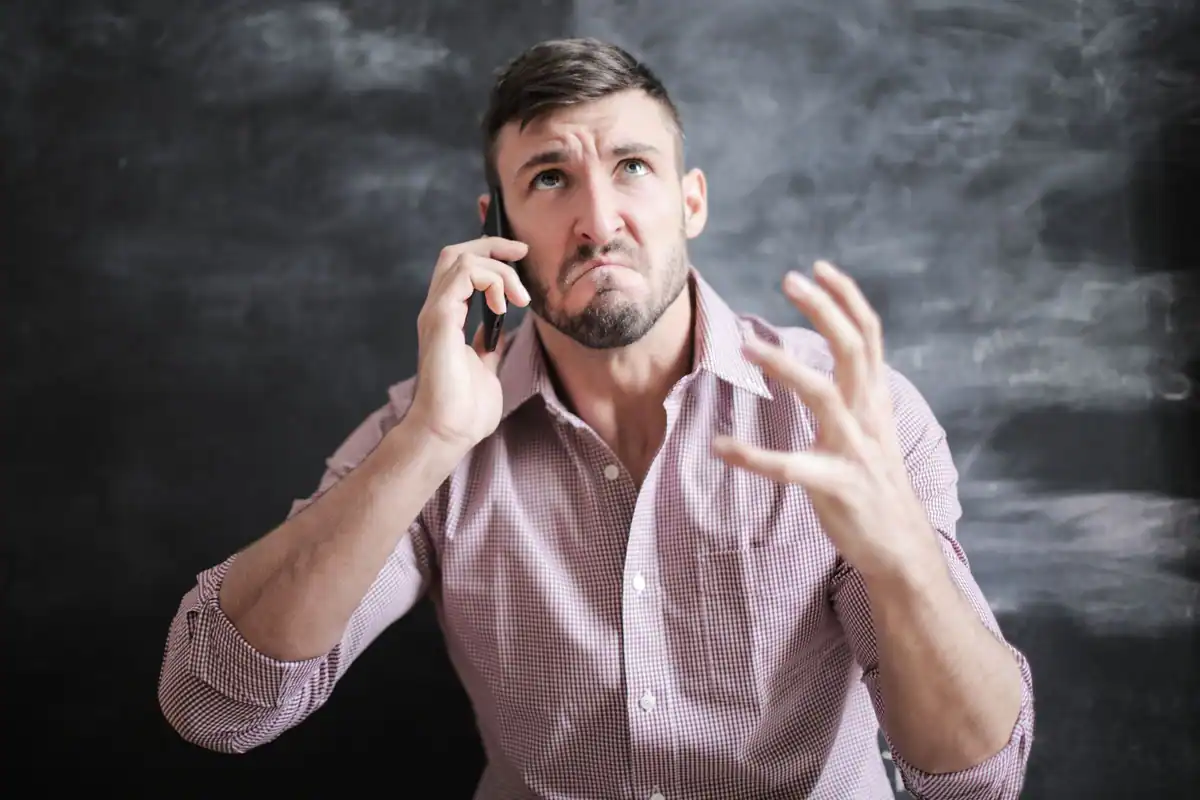 Bărbat îngrijorat vorbește la telefon, cu mâna ridicată și chipul crispat