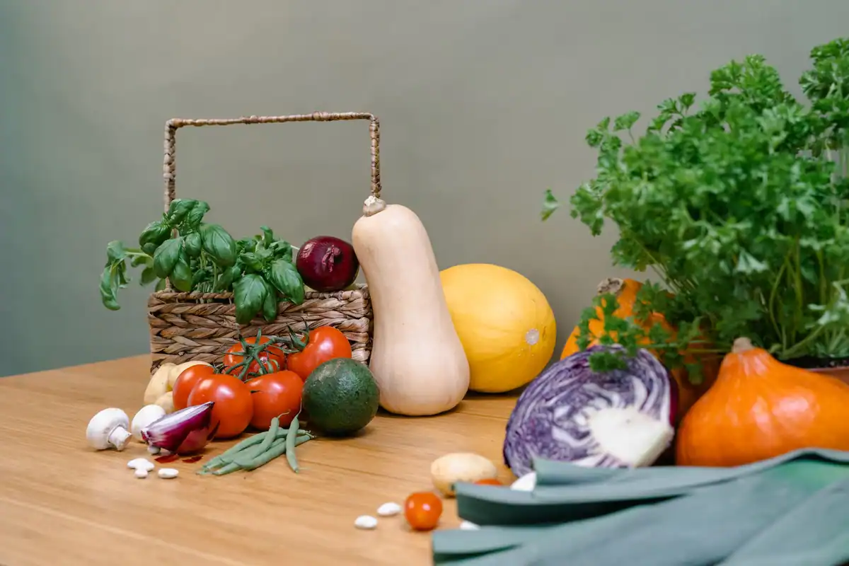 Coș cu legume proaspete, dovleac și plante aromatice, pe o masă de lemn