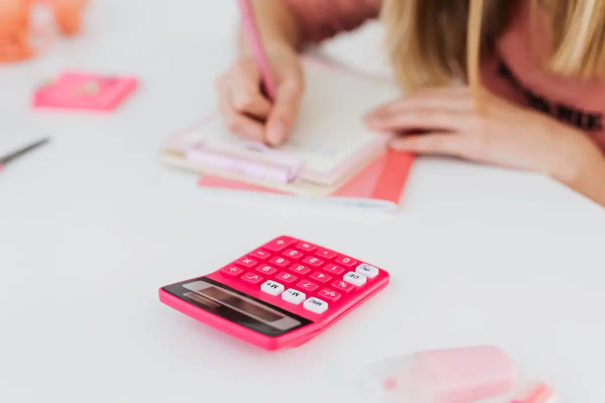 Calculator roz și o persoană care scrie în caiet, pe un birou alb