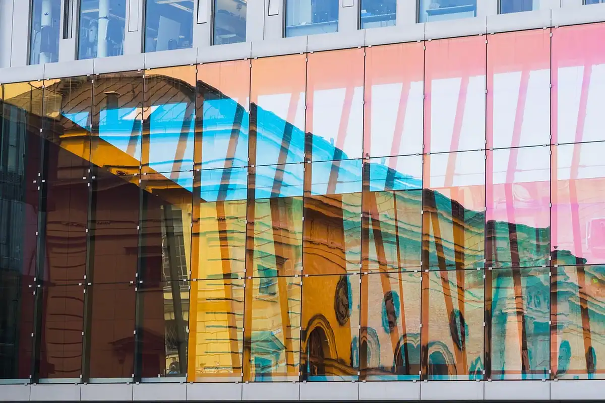 Fațadă de sticlă cu reflexii colorate, care oglindește o clădire veche
