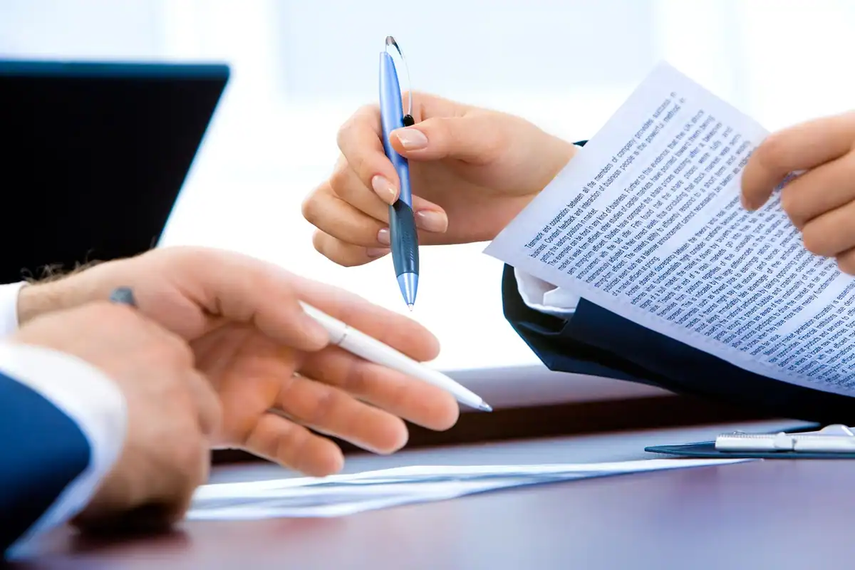 Două persoane la masă discută un contract, cu pix și foi în mâini