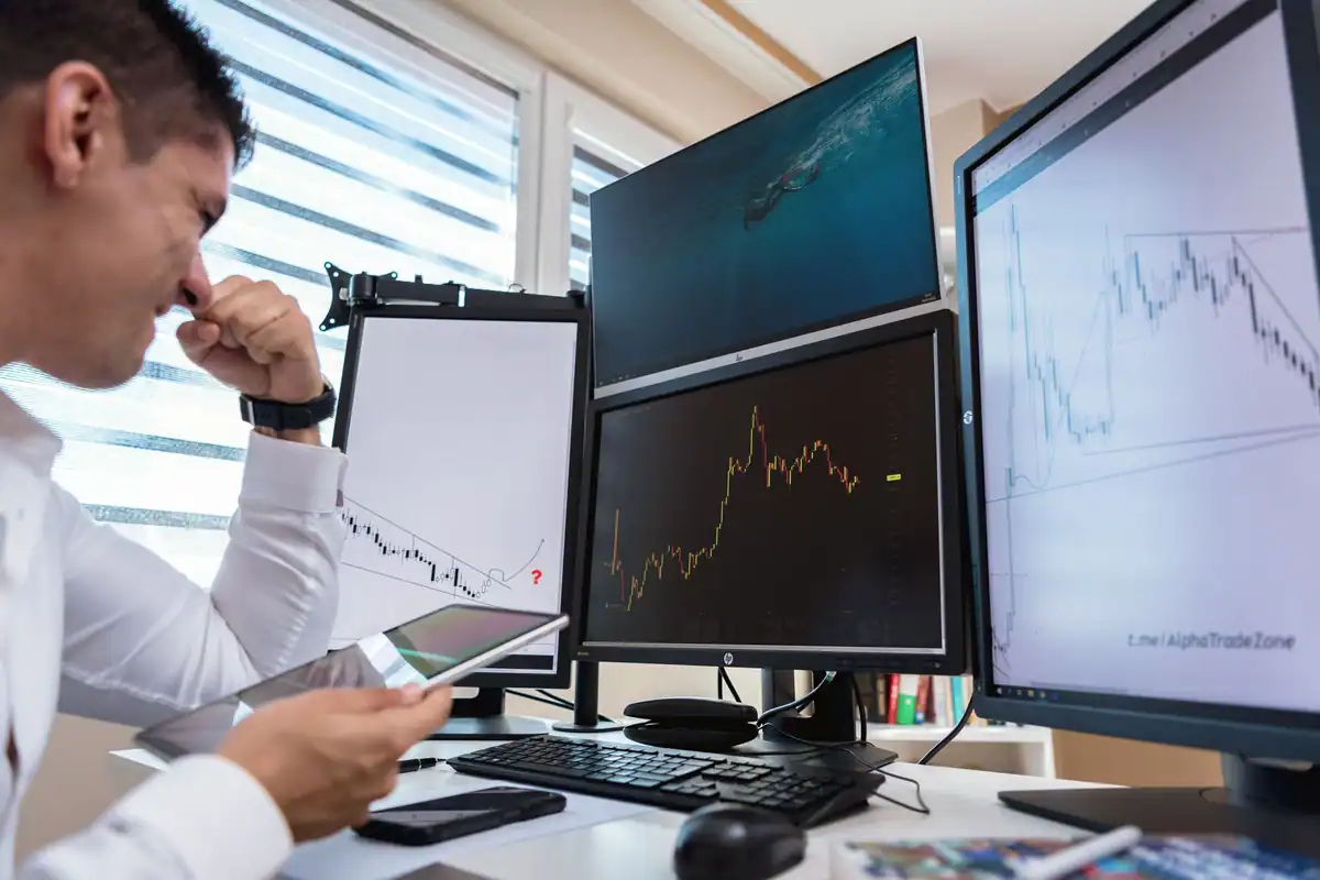 Broker în cămașă albă urmărește grafice bursiere pe mai multe monitoare, într-un birou