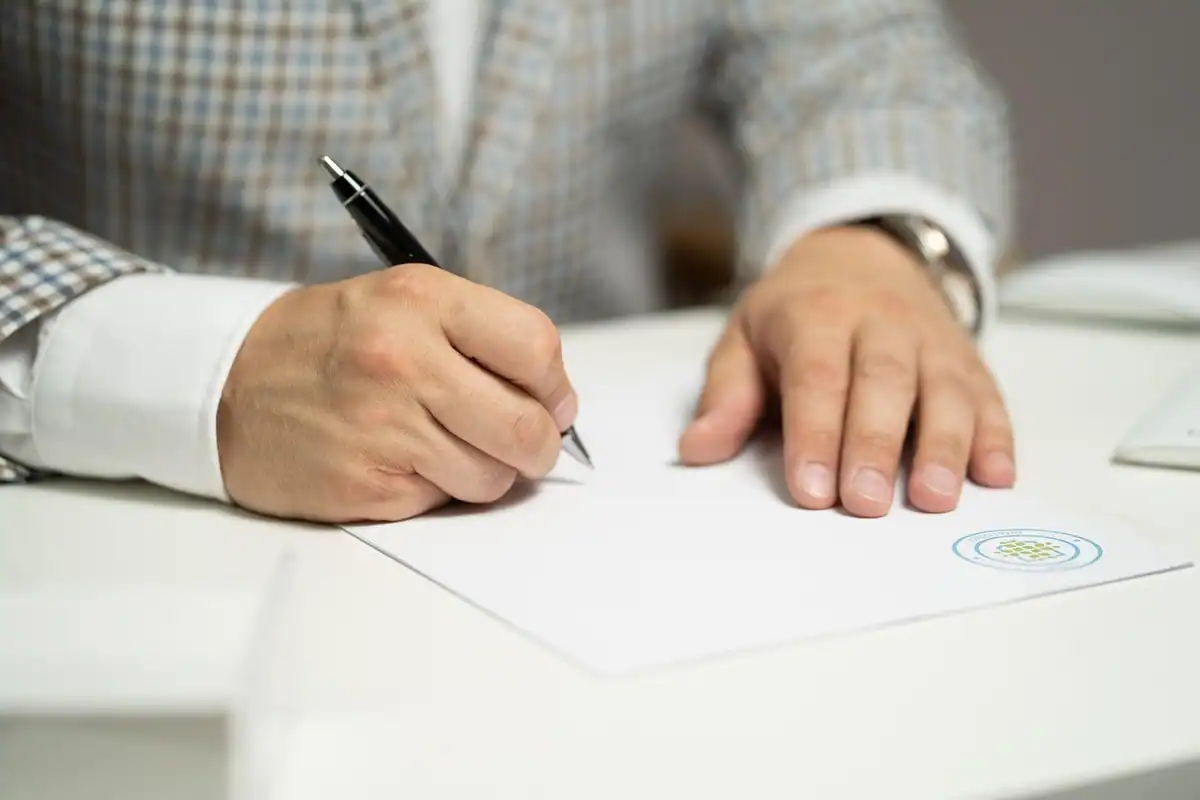 Mâini care semnează un document, cu pixul pe o foaie albă