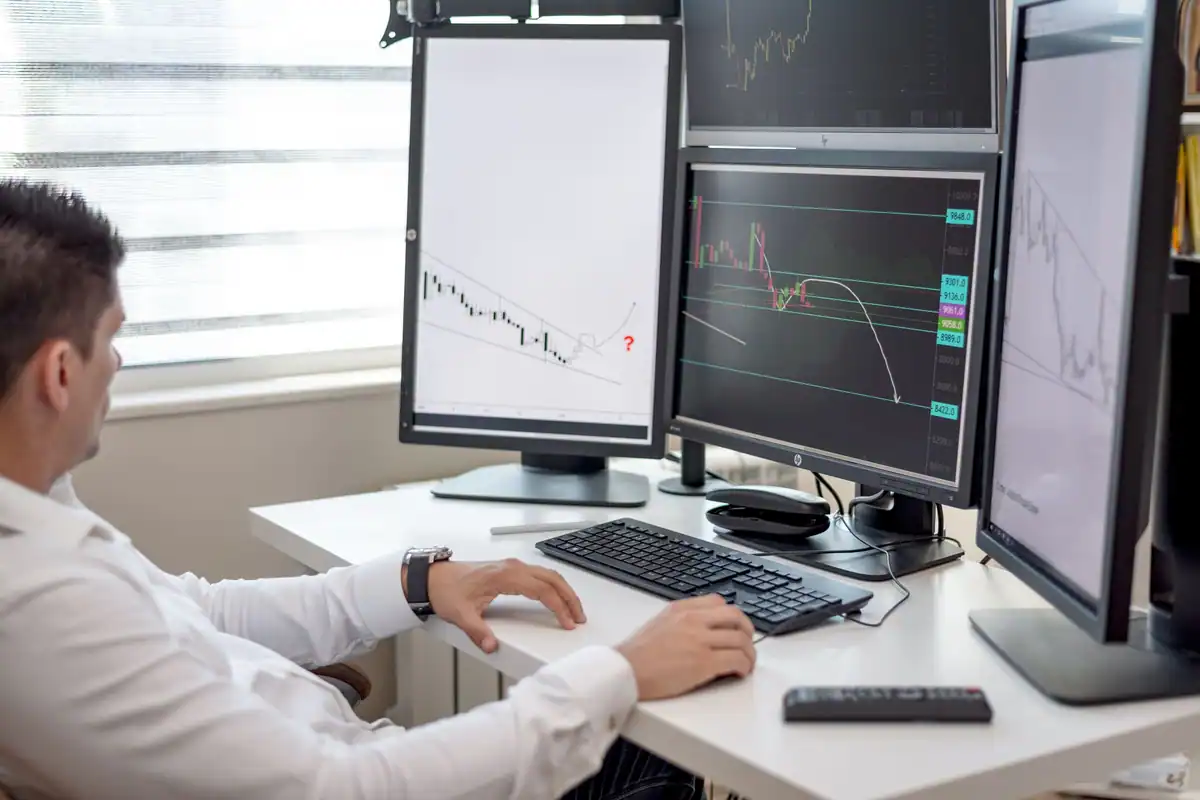 Om de afaceri la birou, analizând grafice financiare pe mai multe monitoare