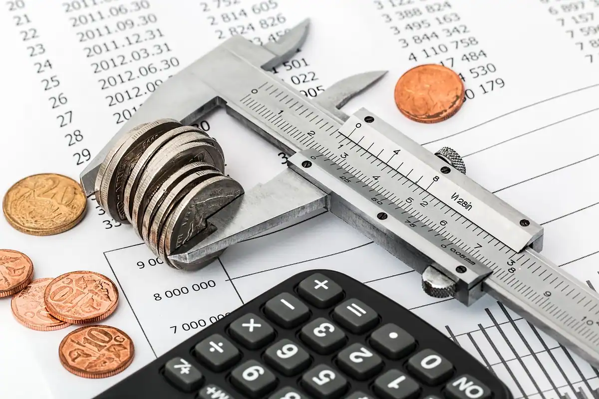 Monede împrăștiate lângă un șubler și un calculator, pe foi cu cifre